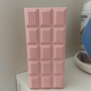 Sweet Tooth parfym av Sabrina Carpenter - Säljer en parfymflaska formad som en chokladkaka i ljusrosa plast. Flaskan heter Sweet Tooth by Sabrina Carpenter och har en unik, geometrisk design som verkligen sticker ut på hyllan. Perfekt för dig som gillar söta och lekfulla dofter.