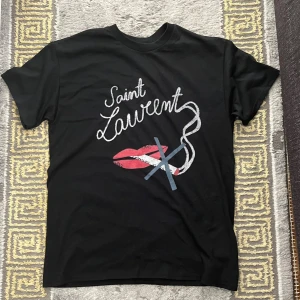 Svart Saint Laurent No Smoking T shirt - Svart t-shirt från Saint Laurent med coolt tryck framtill som visar text, röda läppar och grafiska detaljer. Klassisk rund hals och korta ärmar. Perfekt för dig som vill sticka ut med en ikonisk streetstyle-look.