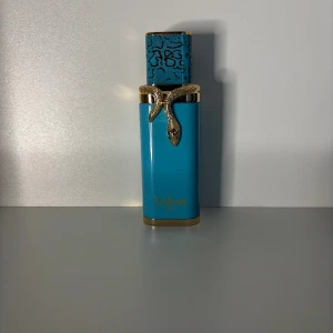 Vulcan fau Sampel - Cool parfymflaska från Vulcan i starkt blå färg med gulddetaljer och en snygg orm runt halsen. Locket har ett mönster i svart och blått som ger extra edge. Perfekt för dig som gillar unika och lyxiga detaljer i din samling.