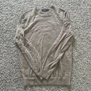 Beige merinoulltröja från Dressmann - Snygg beige tröja från Dressmann i mjuk merinoull. Klassisk rund halsringning och långärmad modell med ribbade muddar. Perfekt för lager-på-lager och enkel att matcha med jeans eller chinos. Säljer då den inte används. Pris kan diskuteras vid snabb affär.