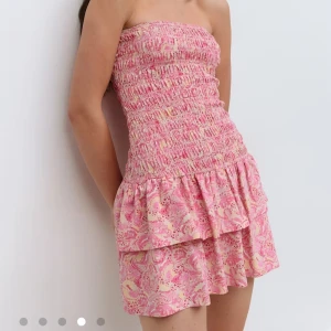 Rosa bandeauklänning med volang - Använd 1 gång. Nypris 400. Supersöt kort bandeauklänning i rosa och ljusgult med smockad överdel och dubbla volanger nertill. Klänningen är ärmlös och har ett paisleyinspirerat mönster, perfekt för varma sommardagar.