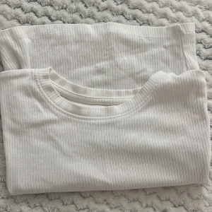 Vit ribbad croppad topp - Säljer en vit croppad topp med ribbad struktur och rund halsringning. T-shirten är kortärmad och sitter tight mot kroppen, perfekt för en clean och enkel look. Passar till både jeans och kjol för en fräsch stil. 