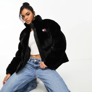 Svart teddyjacka från Tommy Jeans - Tommy Jeans – Svart pufferjacka med fuskpäls från Tommy Jeans med fluffig och mjuk yta. Jackan har hög krage, dragkedja framtill och en broderad logotyp på bröstet. Modellen är loose fit och har långa ärmar. Perfekt för kalla dagar när du vill vara både chill och snygg.