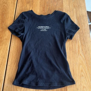 Svart ribbad t-shirt från H&M Divided - Svart ribbad t-shirt från H&M Divided med vit text på bröstet som säger 'FUTURISTIC FEELS'. T-shirten har rund halsringning och korta ärmar. Perfekt för en clean och modern look.