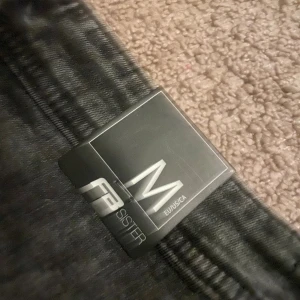 Svarta leggings från FB Sister, M - Säljer ett par svarta leggings från FB Sister i storlek M. De har en hög midja och är i stretchigt material som sitter tajt längs benen. Perfekta för dig som gillar en enkel och clean look med en touch av 90-talsvibe.