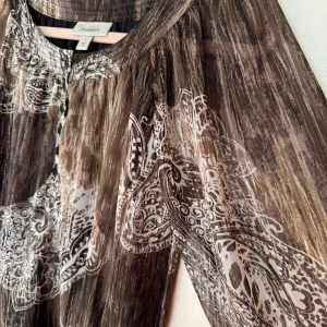 Brun paisleyblus  - Säljer en brunmönstrad blus från Dressbarn i storlek S. Klänningen har ett paisleyinspirerat mönster i vitt, knappar framtill och luftiga trekvartsärmar. Materialet är lätt och transparent, fast blusen har foder. Pyttesmå guldtrådar som liten detalj om man tittar närmare. 