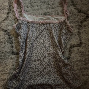 Leopardmönstrad linnetopp med spets - Supersöt linnetopp med grått leopardmönster och ljusrosa spetsdetaljer längs kanterna. Axelbanden är också i spets och framtill finns en liten rosett. 