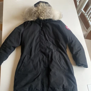 Svart dunparkas från Canada Goose - Säljer en svart dunparkas från Canada Goose med fluffig päls på huvan och klassisk röd logga på ärmen. Jackan har quiltad insida, dragkedja och två fickor framtill. Perfekt för kalla vinterdagar. Den har inga fel alls och är helt ren. Den är i storlek L men passar också M. Pris kan diskuteras. 