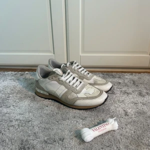 Valentino Rockrunner beige/vit - Snygga Valentino Rockrunner sneakers i beige och vitt med coolt kamouflagemönster. Skorna har detaljer i mocka och skinn, klassisk snörning och ikoniska nitar på hälen. Kommer med extra vita skosnören från Valentino Garavani.