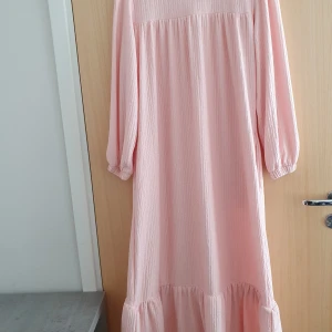 Ljusrosa långklänning med volang -  Babyrosa långklänning med volang nertill och långa ärmar. Klänningen är onesize och aldrig använd 