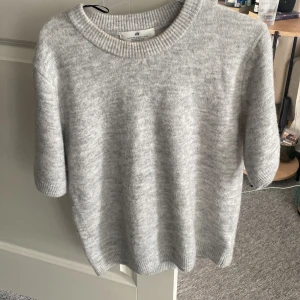 Grå stickad tröja från H&M - Mysig grå stickad tröja från H&M med korta ärmar och rund halsringning. Använt en gång.