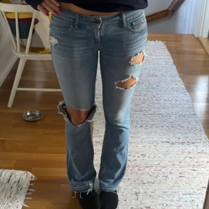 Ljusblåa bootcut jeans Hollister - Ljusblåa jeans från Hollister med låg midja och bootcut. Flera slitningar på benen och vid fickorna. Litet hål längst ned på högra benet, se bild två, som inte märks när man har de på. Annars inga defekter!