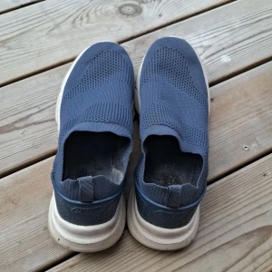 Mörkblå slip-on sneakers från Cruz - Mörkblå slip-on sneakers från Cruz i stickad syntet med vit, tjock sula. Skorna har en sportig look med ventilerande ovandel och elastisk passform utan snörning. Perfekta för dig som gillar bekväma och lätta skor till vardags.