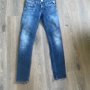 Blå Replay jeans - Snygga blå jeans från Replay med skinny passform och klassisk femficksdesign. Jeansen har ljusa slitningar framtill och bak, samt Replay-logga vid fickan. Materialet är jeans i bomull och de har normal midja. W27 L30
