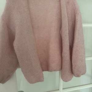 Ljusrosa stickad kofta - Mysig och fluffig ljusrosa stickad kofta med öppen front och långa ärmar. Perfekt för lager-på-lager och ger en avslappnad vibe. Koftan har en enkel design utan knappar eller dragkedja och är supermjuk mot huden.