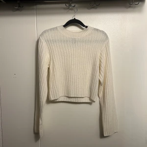 Vit ribbad stickad tröja H&M Divided - Superfin vit ribbad stickad tröja från H&M Divided. Tröjan har en croppad passform, rund halsringning och långa ärmar. Perfekt att styla med jeans eller kjol för en clean look. Materialet är mjukt och skönt mot huden.