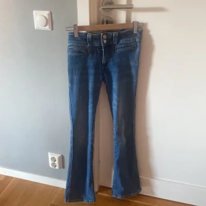 Blå bootcut jeans från H&M - Snygga blå bootcut jeans från H&M med låg midja och justerbar midja. Klassisk femficksmodell i stretchigt denimtyg som sitter skönt och har en lätt utsvängd passform nertill. Perfekta för dig som gillar en retro vibe och vill ha något annat än raka jeans.