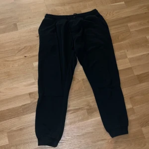 Svarta mjukisbyxor med snörning - Svarta mjukisbyxor med resår och snörning i midjan. Byxorna har muddar vid bensluten och är tillverkade i mjukt material som passar perfekt för chill eller träning. Klassisk och enkel design utan synliga loggor.