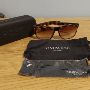 solglasögon OneWear - Snygga solglasögon från OneWear Sweden i klassisk wayfarer-modell. Bågarna har ett brunt sköldpaddsmönster och glasen är tonade i brunt. Kommer med originalfodral, putsduk och tygpåse. Perfekta för att lyfta din stil i solen.