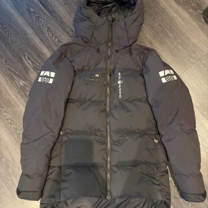 Svart Sail Racing dunjacka med huva - Säljer en svart dunjacka från Sail Racing. Jackan har dragkedja framtill, bröstficka med Sail Racing-tryck och patch med 'Antarctica Expedition'. Perfekt för kalla dagar och riktigt snygg. Jackan är knappt använd och i nästan nyskick. Nypris ca 4000kr hos stadium. (Pris kan diskuteras)