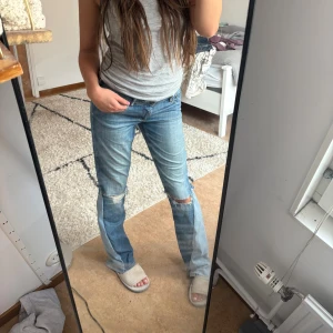 Blå bootcut jeans med slitna knän - Säljer ett par blå jeans med bootcut passform och slitna detaljer vid knäna. Jeansen har klassisk femficksdesign, låg midja och är tillverkade i denim. Perfekta för dig som gillar en avslappnad och trendig look. De är ursprungligen skinny acne jeans men sytt om dom så dem blir mer bootcut! Så lite hemsytt därav priset men skit snygga ändå
