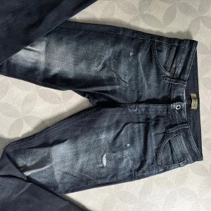 Jack n Jones med slitningar 29/32 - Snygga svarta jeans från Jack & Jones med slitna detaljer och lätt tvättad look. Klassisk femficksmodell med raka ben och normal passform. Jeansen är gjorda i bomull med lite stretch för extra komfort.