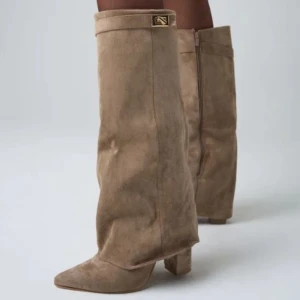 Beige mockastövlar med klack - Snygga beige stövlar i mocka med bred, hög skaft och markerad klack. De har spetsig tå, dragkedja och en diskret gulddetalj upptill. Perfekta för att lyfta din outfit med en trendig touch. Använda 1 gång. Hör av dig om du har några frågor! 🫶🏼💕