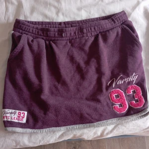 Vinröd kortkjol Red & Blue - Sportig vinröd kortkjol från Red & Blue med grå kantdetaljer, broderad text och siffran 93 framtill. Mjuk bomullskvalitet, elastisk midja och praktiska fickor. Perfekt för en avslappnad och cool look.