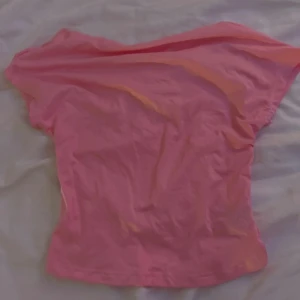 Rosa topp med öppen rygg - Säljer en rosa topp i mjuk bomull med korta ärmar och en snygg öppen rygg. Toppen har en enkel, figurnära passform och är perfekt för dig som vill ha en basic men ändå trendig look. Färgen är riktigt poppig och passar till många olika outfits. Aldrig använd 