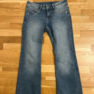 Blå bootcut jeans med utsvängda ben - Snygga blå jeans med bootcut-modell och klassisk femficksdesign. Jeansen har en lätt tvättad look och utsvängda ben, vilket ger en retro vibe. Tillverkade i mjukt denimtyg med normal passform och midja. Perfekta för dig som gillar en avslappnad men trendig stil.