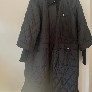 Svart quiltad jacka från Freequent - Quiltad svart jacka från Freequent i storlek XL. Jackan har lång ärm, dragkedja framtill och tryckknappar på fickorna. Den har en loose passform och är perfekt för höst och vinter. Snyggt rutmönster och klassisk look som funkar till många outfits.