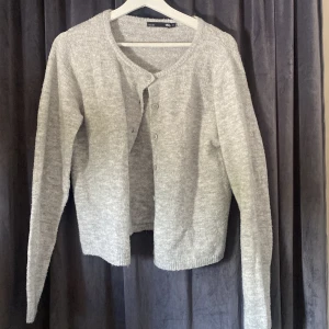 Ljusgrå kofta från 157, storlek S - Mysig ljusgrå kofta från 157 med rund halsringning och knappar framtill. Tillverkad i en mjuk blandning av akryl, polyester och elastan. Perfekt att slänga över en t-shirt eller linne för en chill look. Långärmad och enkel att matcha med det mesta.