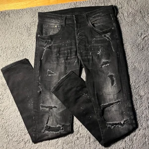 Svarta slim fit jeans med slitningar - Säljer ett par svarta slim fit jeans från Denim med coola slitningar och färgstänk. Storleken står 31 men passar som 30.