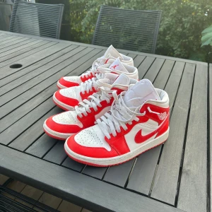 Nike Air Jordan 1 Mid röd/vit - Nike Air Jordan 1 Mid sneakers i rött och vitt med klassisk Jordan-logga på sidan. Skorna har snörning, perforerad tå och är tillverkade i skinn och syntet. Snygg kontrast mellan de röda och vita panelerna samt ikonisk Swoosh på sidan.. säljer båda för 600kr
