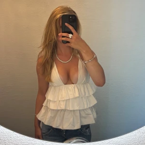 Vit volang topp med djup v-ringning - Säljer en vit linnetopp med flera lager volanger och djup v-ringning. Toppen är sydd av mig och passar runt s. Ställ gärna frågor! 🩷💕