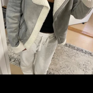 Grå teddyjacka med dragkedja - Snygg grå teddyjacka från Gina Tricot med vit fuskpäls på krage, ärmslut och nederkant. Jackan har en schysst asymmetrisk dragkedja och två fickor med dragkedjor. Perfekt för kalla dagar och ger en cool vibe till din outfit.