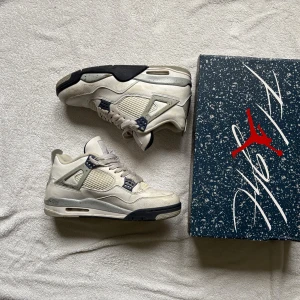 Nike Air Jordan 4 Retro White/Midnight Navy - Nike Air Jordan 4 Retro i färgen White/Midnight Navy. Klassiska sneakers med vit ovandel i skinn, meshpaneler och detaljer i marinblått. Grå och svarta inslag på sulan, ikonisk Jumpman-logga på plösen. Snygg siluett och coola detaljer för dig som gillar streetwear.