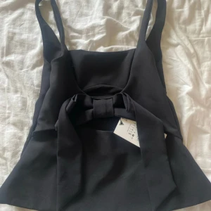 Svart topp med rosett Zara - Supersnygg svart linnetopp från Zara med breda axelband och en stor rosett framtill. Toppen har en lätt utsvängd form och är perfekt för att skapa en chic look. Har prislapp kvar 