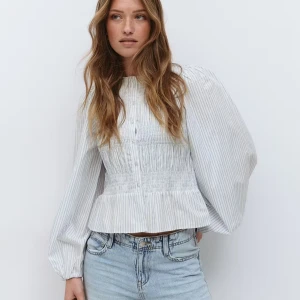 Blåvit randig blus med puffärm - Supersöt vit blus med tunna blå ränder, puffiga långärmar och smockad midja. Blusen har knappar framtill och en liten volang nertill som ger en feminin touch. Perfekt till jeans eller kjol för en fräsch look. Helt oanvänd och slutsåld på Gina Tricot. Bara testad en gång. Säljer då den är för liten på mig. Storlek xs.