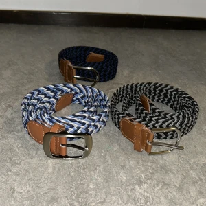 Flätat bälte - Säljer tre snygga flätade bälten med bruna skinn-detaljer och metallspännen. Ett bälte är blått och vitt, ett är svart och grått, och ett marinblått. 