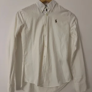 Vit figursydd skjorta från Ralph Lauren slim fit - Vit skjorta från Ralph Lauren i slim fit-modell och figursydd. Skjortan är tillverkad i 100% bomull och har långa ärmar, knappar framtill och broderade loggan på bröstet. Xs-xxs