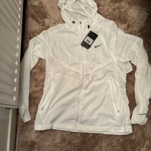 Vit Nike Miller strl M - Snygg vit vindjacka från Nike med huva och dragkedja framtill. Jackan har två fickor med diskret Nike-logga på bröstet. Kom privat för fler bilder eller frågor aktiv varje dag‼️‼️
