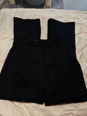 Svarta kostymbyxor  - Snygga svarta kostymbyxor  Byxorna har två bakfickor och är tillverkade i ett slätt tyg som ger en stilren look. Perfekta för dig som gillar minimalistisk stil och vill ha ett par dressade byxor.defekter i bilder 2 sista