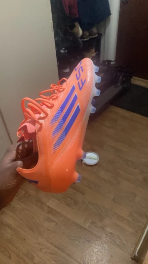 Adidas F50 orange fotbollsskor - Säljer ett par Adidas F50 fotbollsskor i en riktigt fet orange färg med blå detaljer och vita linjer. Skorna har snörning, platt sula med dobbar och är tillverkade i syntetmaterial. Perfekta för dig som vill sticka ut på planen och få grymt grepp. Med väska också