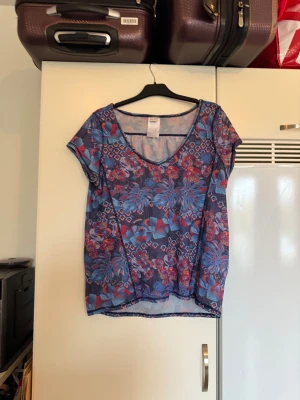 Blommig mesh blus från Odd Molly - Säljer en färgstark meshblus från Odd Molly med blommigt mönster i blått, rött och lila. Blusen har v-ringning, korta ärmar och är lätt transparent. Perfekt för dig som gillar att sticka ut med coola prints och luftig känsla. Från märket Odd Molly. Storlek 3 som enligt deras storleksguide motsvarar en L. Mycket fint skick, jag hittar inga synliga anmärkningar eller defekter. 