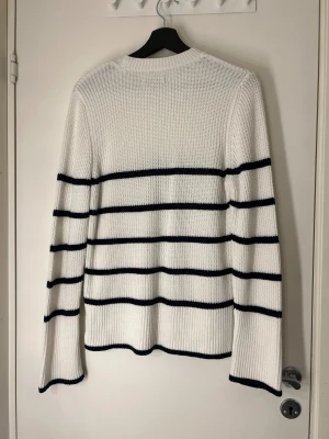 Vit stickad randig tröja Anna Field - Vit stickad tröja från Anna Field med svarta horisontella ränder. Tröjan har rund hals, långärmad passform och ribbade muddar vid ärmslut och nederkant. Perfekt för dig som gillar klassisk och chill stil.