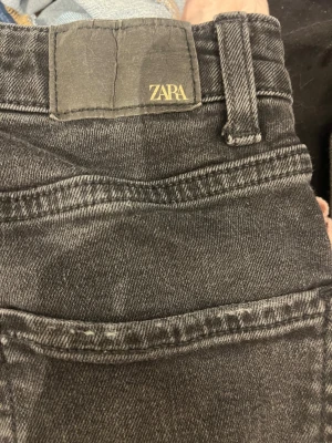 Svarta jeans från Zara - Svarta jeans från Zara med skinny passform och råa, fransiga benslut. Klassisk femficksmodell med knapp och dragkedja fram. Jeansen har en mörk tvätt och är tillverkade i stretchigt denim för en tajt och bekväm känsla.