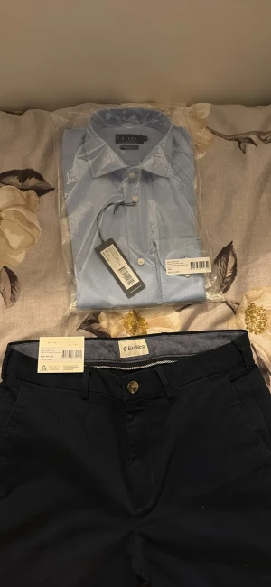 Navyblå chinos från EastWest W31/L30 - Snygga navyblå chinos från EastWest i slim fit med stretch för extra komfort. Klassisk design med knappstängning och bälteshällor, perfekta för en clean och stilren look. Passar dig som gillar smalare passform och vill ha ett par mångsidiga byxor.
