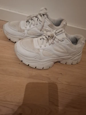 Chunky vita sneakers från Graceland - Säljer ett par chunky vita sneakers från Graceland i storlek 37. Skorna har en kraftig plattformssula, snörning och detaljer i mesh och syntetmaterial. Perfekt för dig som gillar en sportig och trendig look med extra höjd.