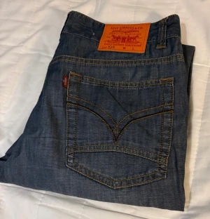 Levi's 523 Straight blå jeans - Säljer ett par Levi's 523 Straight jeans i klassisk blå tvätt med snygga slitningar framtill. Jeansen har raka ben, fem fickor och kontrastsömmar. Märkespatch i läder baktill och Levi's-röd etikett på bakfickan. Perfekt passform och tidlös look.